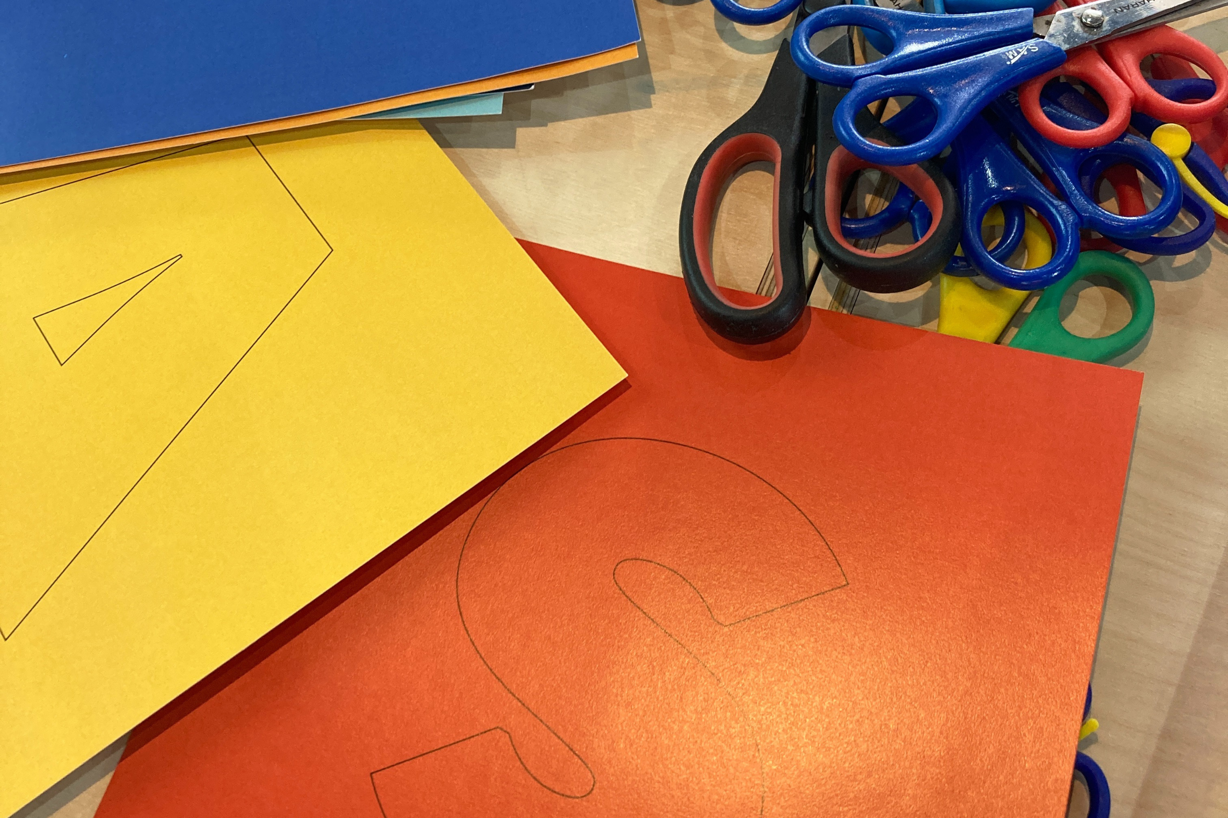 Letters traced onto coloured card, next to a handful of scissors